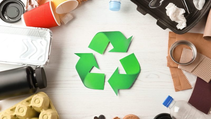 Recycling symbol and different garbage on wooden background, top view